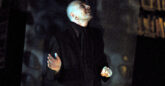 A male storyteller stands on a dark stage and looks up at the sky