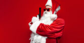 Father Christmas holding a gun in an upwards direction in front of a red background